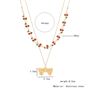 Vue détaillée du collier double épaisseur en acier doré avec pendentifs cerise et nœud