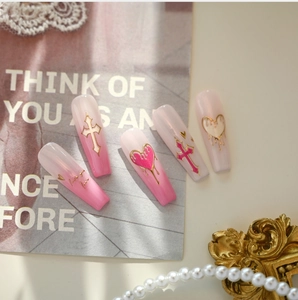 Detail of pink gradient coffin press-on nails with metallic hearts and crosses