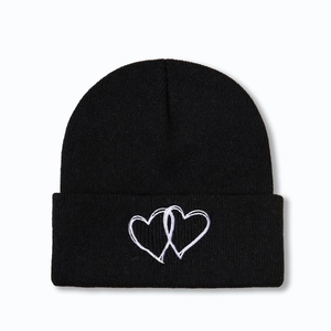 Détail de la broderie à deux cœurs entrelacés sur un bonnet en maille noire d'hiver
