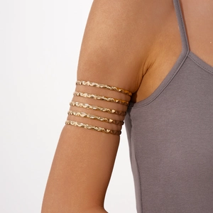 Detail of a golden five-layer wavy metal arm cuff on model upper arm with textured finish