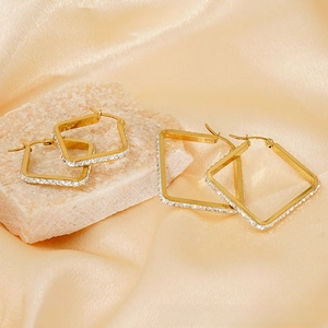 Detail of square gold earrings with white crystals on a beige stone and silk background