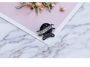 Detail of Let's Seek black crystal ball enamel pin on marble background with dry flowers