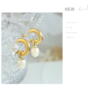 Macro detail of gold C-shape earrings with drop pearls and sparkling zircon accents