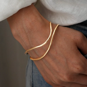 Detail of minimalist wavy double-layer gold bangle worn on wrist with elegant polished finish
