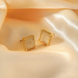 Close-up of square gold-tone stud earrings with pavé-set zircons on champagne silk