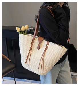Straw tote bag with leather straps and tassel detail shown on a model for casual beach style