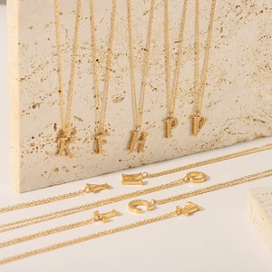 Gold letter necklace with white zircon pendants on a light stone background