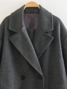 Detail of dark grey double-breasted coat featuring classic lapels and wool texture