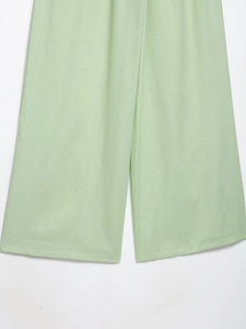 Détail du pantalon large en lin vert clair montrant la texture et le drapé du tissu