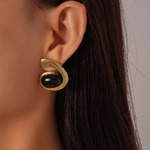 Close-up of vintage golden geometric earrings featuring a black oval cabochon stone on model
