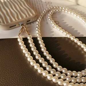 Crossbody pearl phone lanyard with gold metal clasp on a textured wavy phone case