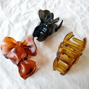 Close-up of matte amber and black bow-shaped hair claws on white fabric texture