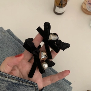 Pair of black velvet bow hair ties with heart crystal and pearl charms held in hand