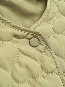 Detail of olive green quilted jacket featuring round neckline and matte button closure