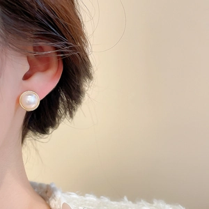 Close-up of elegant gold pearl stud earrings with textured bezel on a model's ear