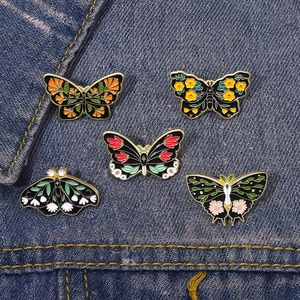 Detailed view of five colorful butterfly enamel pins pinned on a blue denim jacket fabric