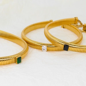 Three gold snake chain bracelets with emerald-cut crystals in green, white, and black colors