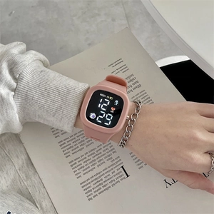 Close-up of pink square digital watch with silicone strap worn against a book background