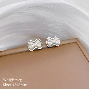 Close-up of silver bow stud earrings with white pearl inlay on brown leather box