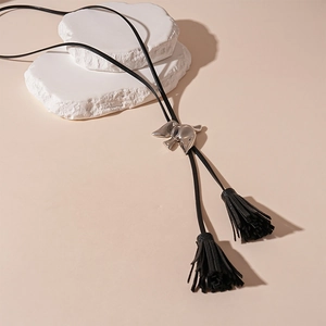 Detail of silver bird-shaped slider and black leather tassels on a long necklace