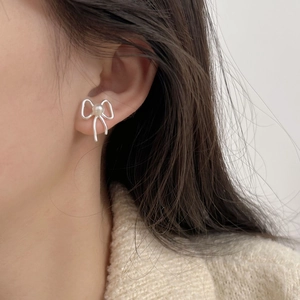 Close-up of a silver bow knot earring with a white pearl on a model's ear