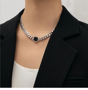 Close-up of thick silver chain necklace with black square pendant on model outfit