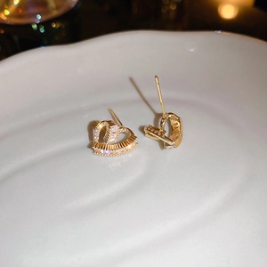 Macro view of gold-plated heart stud earrings with sparkling cubic zirconia on ceramic