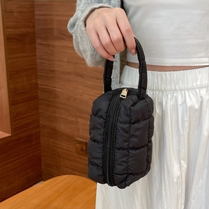 Chic black quilted makeup bag with top handle and zipper closure held by a model