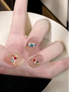 Macro detail of press-on nails with colorful rhinestones and pearls on nude base