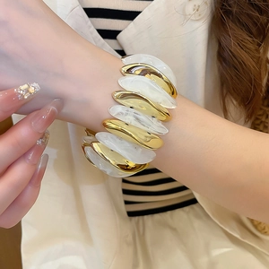Macro shot of gold metal and white marble acrylic teardrop modules on wide bracelet