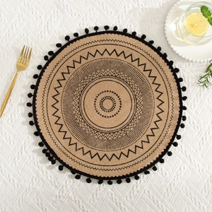 Detail of round jute placemat featuring black geometric patterns and fringe tassels