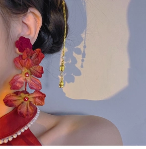 Detail of red rose earrings with long golden tassels and pearls on a model