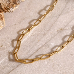 Close-up of gold stainless steel paperclip link chain on a textured stone surface