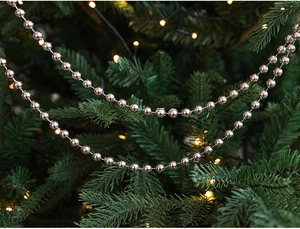 Close-up of rose gold bead chain garland wrapped around green Christmas tree branches