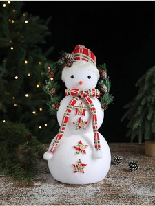 Close-up of white flocked snowman with red-green plaid scarf on snowy wood base