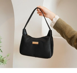 Close-up of black pebble leather underarm bag with gold metal plate and zipper detail