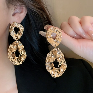 Close-up of golden geometric textured drop earrings with hammered finish and vintage style
