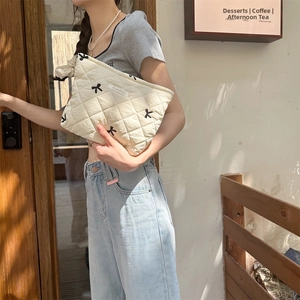 Close-up of a quilted cream makeup bag with embroidered black bows held by a model