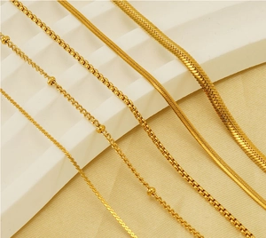 Detail of 18K gold-plated stainless steel snake and bead chains on a beige surface