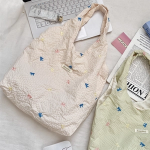 Détail de nœuds colorés brodés sur un sac cabas en tissu gaufré aux tons doux et naturels