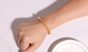 Close-up of golden Franco wheat chain bracelet worn on wrist over a stone background