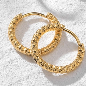 Macro shot of gold hoop earrings with embossed star texture on white stone background
