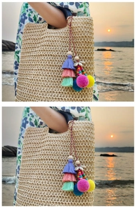 Detail of colorful boho tassel charm with pom poms on a beige straw beach tote bag
