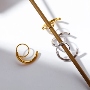 Macro detail of minimalist gold and silver spiral hoop earrings on wooden stand
