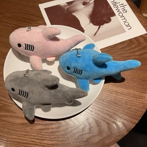 Close-up of three mini plush shark keychains in pink, blue, and grey on a white plate