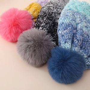 Close-up of cable knit texture and large fluffy faux fur pom-poms on children winter hats