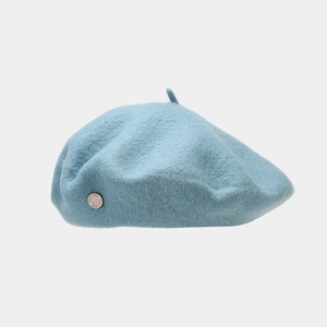 Detail of light blue wool beret featuring a classic silver metal side logo and soft texture