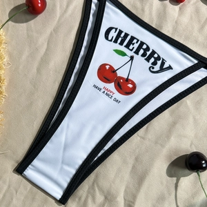 Detailed view of white bikini bottoms featuring cherry print and graphic lettering