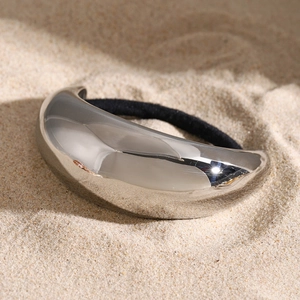 Macro detail of silver polished metal hair tie accessory on a textured sand background