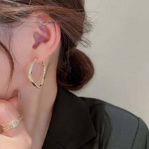 Macro detail of gold-plated twisted geometric earrings and matching ring with zircons